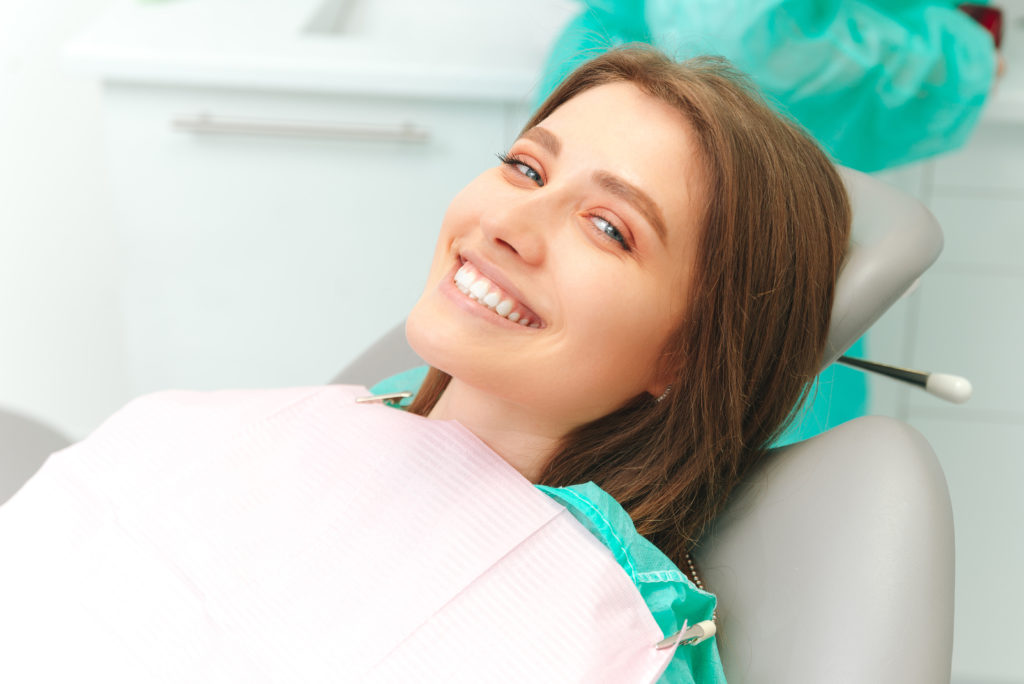 Ecstatic young woman is wide smiling while sitting on the dentist chair. Close up photo with copy space.